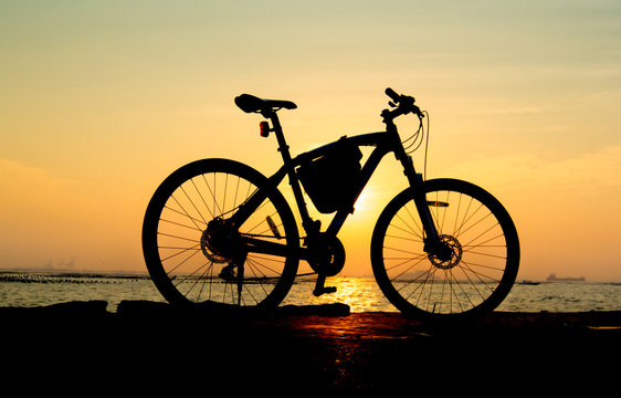 Silhouette of mountain bike at sea with sunset sky background