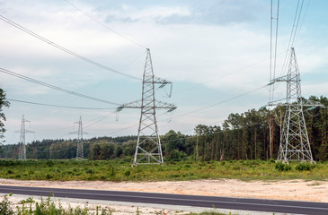 Fototapeta premium Electricity pylons with wires on a background of forest and roads.