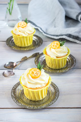 Cupcakes with cream cheese on white wooden table.