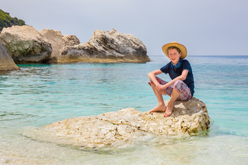Boy with hat sitting on rock in sea