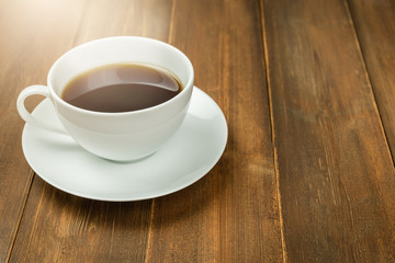 Coffee cup on wood table in morning sunlight.