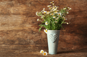 Vase with bouquet of fresh chamomiles on wooden wall background