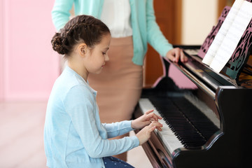 Small girl learning play piano with teacher