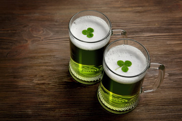 Glasses of green beer with clover leaves on wooden background