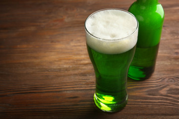 Glass of green beer and bottle on wooden background