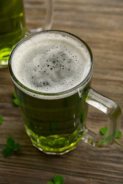 Glass of green beer with clover leaves on wooden background