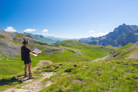 Hiker reading trekking map while resting at panoramic mountain spot. Outdoors activities, summer adventures and exploration on the Italian French Alps. Expansive view from the top.