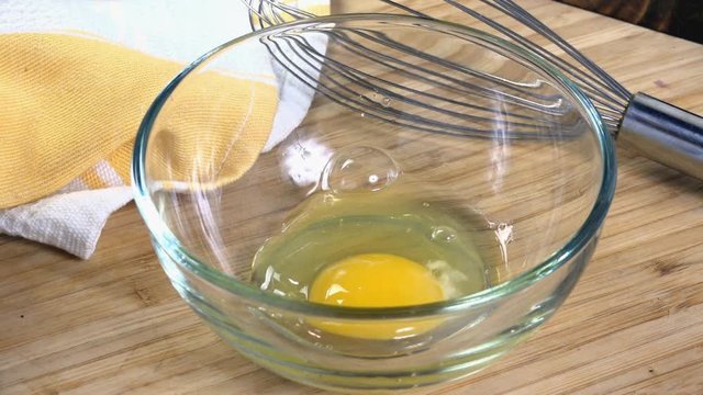 A raw egg dropping into a bowl in slow motion
