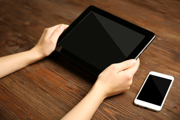 Mobile phone and female hands using tablet, on the wooden background