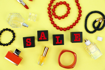 Black wooden cubes with perfumes and accessories on yellow background. Sale concept