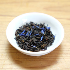 Dried loose leaf tea - Earl Grey cream, black tea leaves with blue cornflower petals. In a white dish on a rustic wooden background. Very shallow depth of field.
