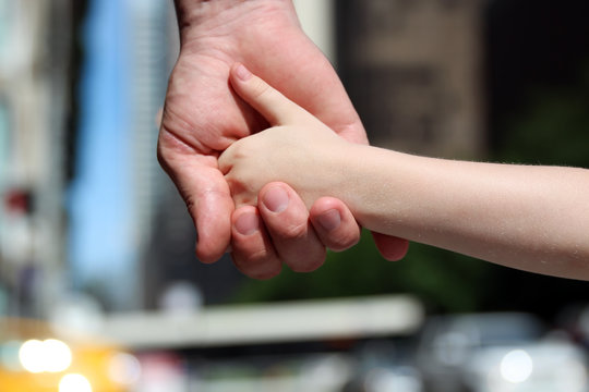 a father holds the hand of a small child outdoor