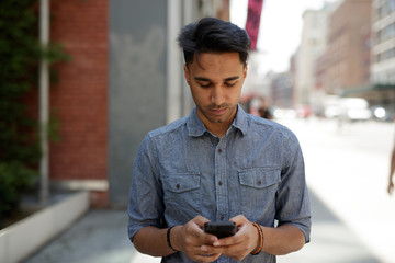 Young Indian man in city texting cell phone