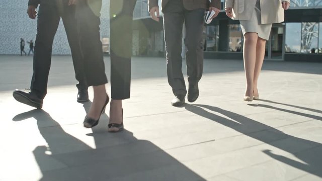 Legs of four business people walking on the pavement in front of office building