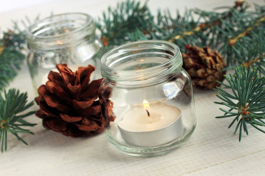 Handmade simple winter home decoration. Candle in glass jar, evergreen conifer twigs, cones. Natural festive scents. 
