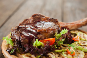Roasted steak on bone, with red topping, with vegetables on wooden background, closeup