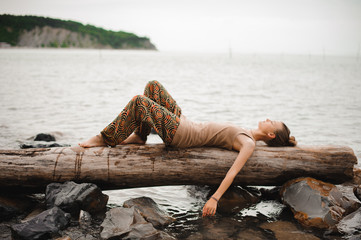 Dreaming young woman is lying on the log at the water