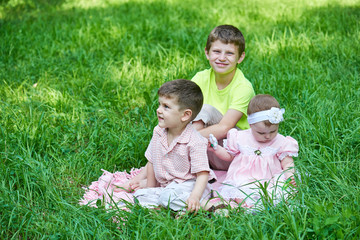 Naklejka na ściany i meble Three children sit in grass, playing and having fun.