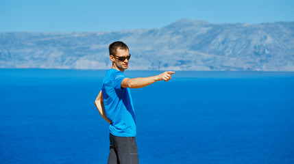 man stands on a blue sea and sky background at early morning. man shows somewhere at right by right hand