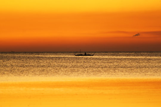 Fototapeta Small boat with fisherman swim on sea. Beautiful bright yellow background of sunset. Water surface scintillates on the sunset shine.
