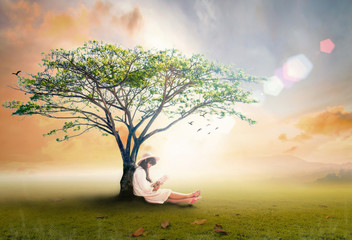Read a book day concept: Asian girl reading fantastic book under big tree in autumn sunset...