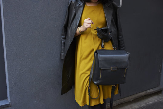 Midsection of woman using cell phone while leaning against wall