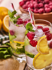 On wooden boards is cocktail glass with berries lemon and ice cubes. Alcohol country cocktail number ninety two with clay bowl raspberries with mint and ice cubes. Country life cocktail.