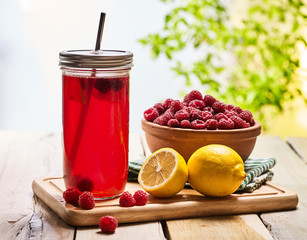 On wooden boards is ice cold drink glasses with raspberry lemon cocktail . Country ice cold drink number ninety three with raspberry clay bowl outdoor with green tree.