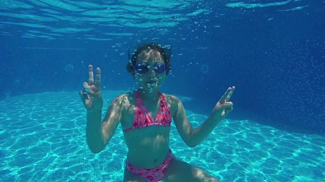 Underwater view Young girl swimming in pool and saying OK in front of camera
