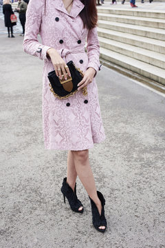 Woman in a pink coat and black high heels holding a handbag