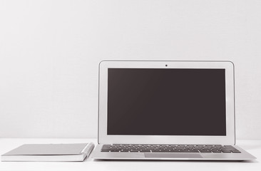 Closeup computer notebook on blurred white wood desk and cream color wallpaper wall in room texture background , beautiful work place interior of house concept in black and white tone