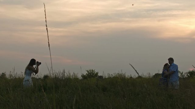 Female photographer showing photos for adult couple during fashion photo shoot outdoor, silhouette, wide angle