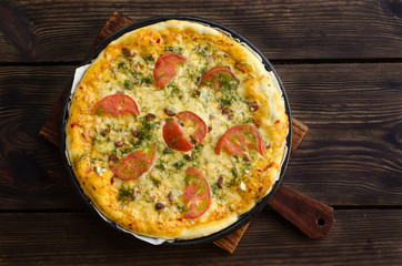 Homemade pizza with cheese and vegetables on wooden background.