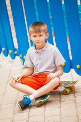 Boy sitting on a skateboard on the background of blue fence