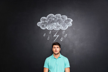 Surprised astonished man standing under raincloud drawn on blackboard background