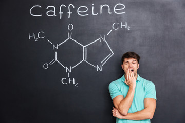 Exhausted fatigued man yawning over chalkboard with drawn caffeine molecule