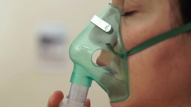 Close up side shot of a woman using a breathing mask nebulizer treatment to help her with a respiratory or lung illness.