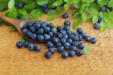 Juicy mature berries of bilberry in in a wooden spoon on a wooden surface.