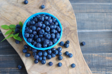 Berries of ripe juicy bilberry in a blue small  plate on a wooden table.