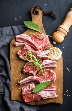 Raw uncooked lamb chops with herbs and spices on rustic wooden board over dark  background