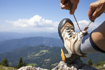 Hiker tying boot laces on rock, high in the mountains, space for text