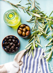 Two bowls with pickled green and black olives, olive tree sprigs, fresh homemade oil over blue Turquoise background
