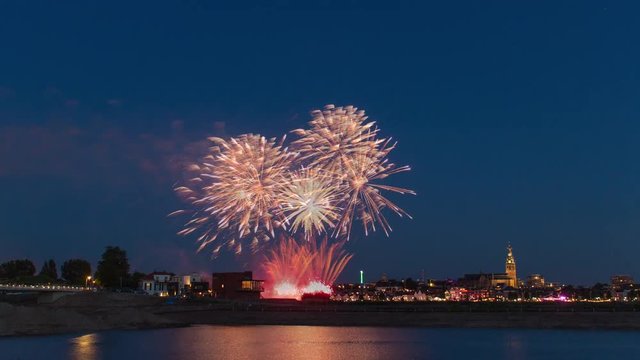 Colorful fireworks above city skyline reflecting in pond, 4K time lapse