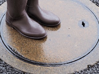 雨に日に水たまりの上いを歩く長靴を履いた女性