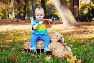 little boy sitting on a basket and holding yellow autumn leaves