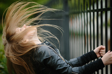 beautiful cool girl making trick with her hair in black leather jacket over grunge fence