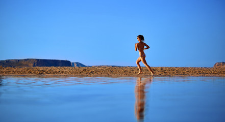 beautiful athletic woman dressed in bikini running on the beach along the sea front