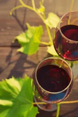 Fotobehang Two glasses of red wine and grape leaves on a wooden surface in beams of the setting sun © isavira