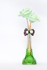 Two green decorative roses in glass vase, on white background with a ribbon