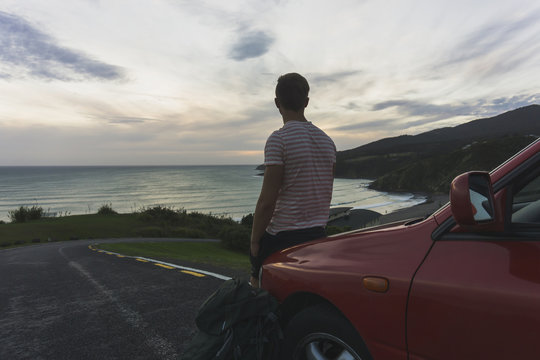 Back view of tourist leaning against car looking to the sea